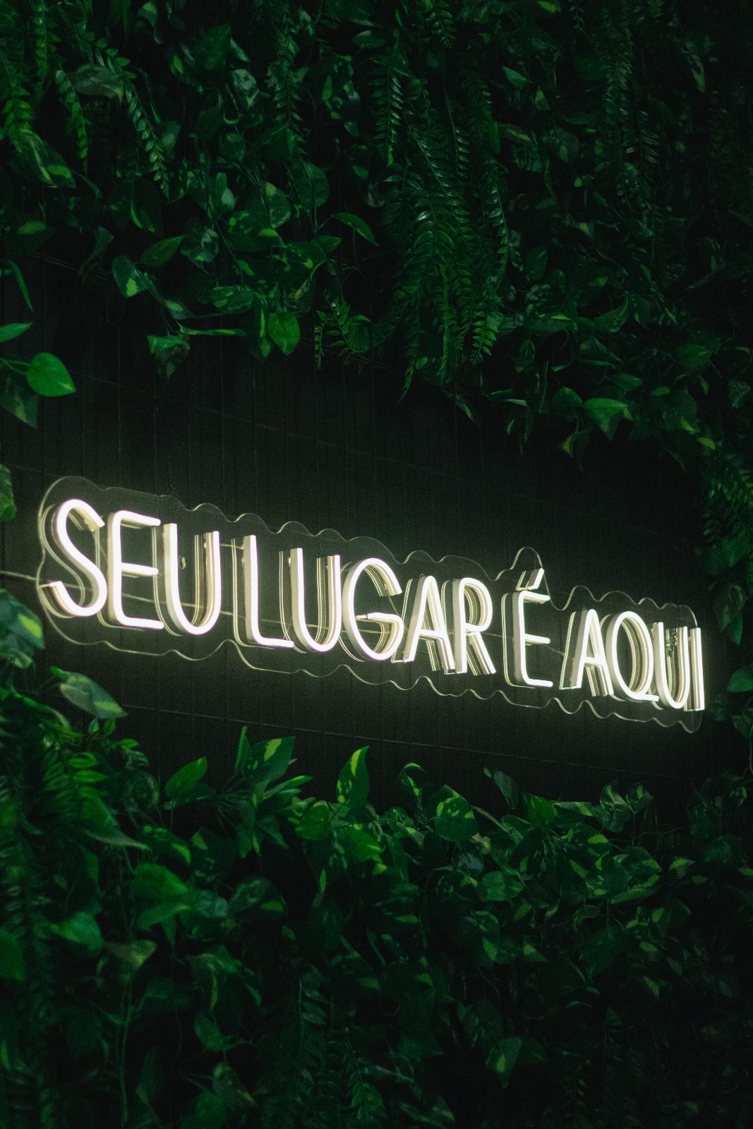 Letreiro luminoso “Seu lugar é aqui” na parede de plantas da igreja